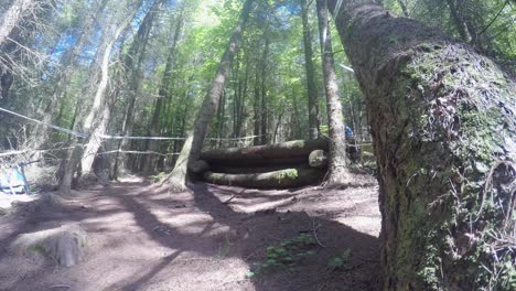 Mountain-Biker-riding-downhill-at-high-speed-in-forestry-track,-riding-over-build-up-log-jump