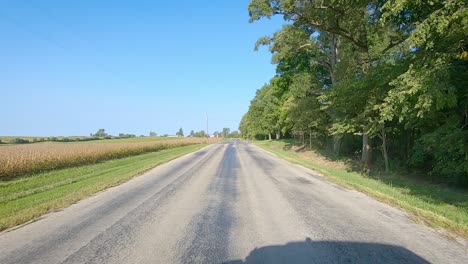 pov driving on rural county road with no center line past maturing fields, farmyard, and bicyclist in rural iowa on a sunny early autumn day