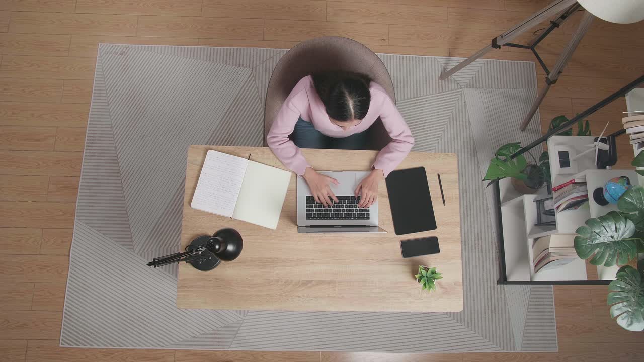 Top View Of A Woman Stretching While Sitting At The Wooden Desk Typing On A Laptop At Home
