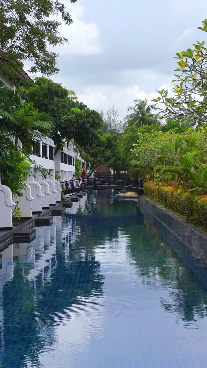 Family strolls above sparkling water, surrounded by greenery and elegant resort buildings, enjoying a relaxing vacation in Thailand