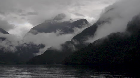 slow motion static footage of misty and cloudy mountains in doubtful sound with water in foreground - patea, new zealand