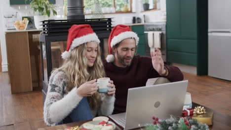 Vielfältiges-Paar-Mit-Weihnachtsmützen,-Das-Einen-Laptop-Für-Einen-Weihnachtsvideoanruf-In-Zeitlupe-Verwendet