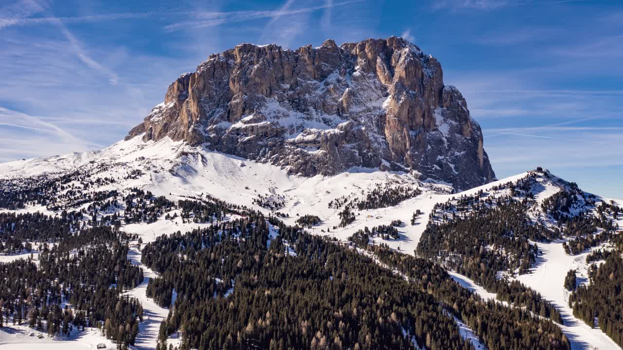 The Saslonch, Sassolungo or Langkofel - the highest mountain of the Langkofel Group in the Dolomites, Italy.  It is towering above the snow-covered valley.  Skiiers on the slopes. Blue sky.  Sunny.