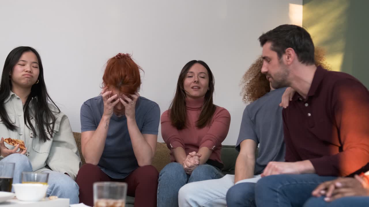 Diverse friends watching match on couch with drinks and food
