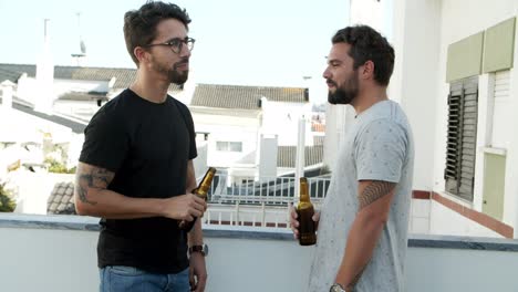 Two-handsome-young-man-clinking-beer-bottles-and-drinking