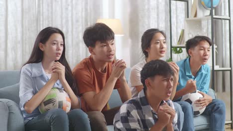 asian teenagers cheering and watching football game on tv and disappointed at home