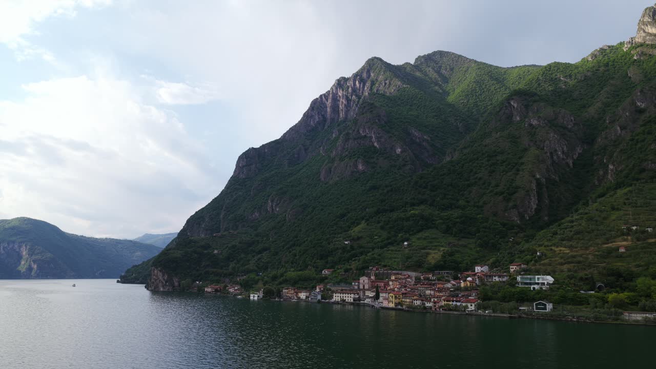 Marone village between green mountains and calm waters of Lake Iseo, Lombardy, Italy. Aerial drone lateral view