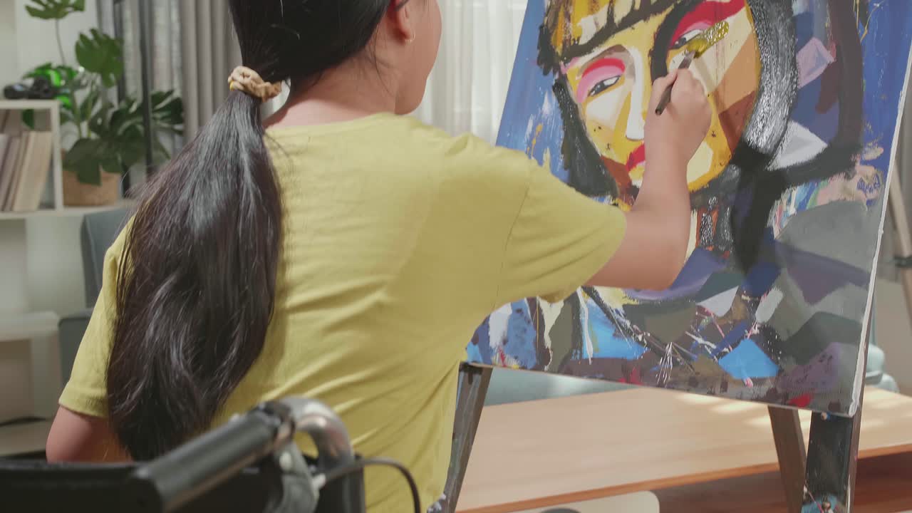 Hind View Of An Asian Artist Girl In Wheelchair Thinking And Painting A Girl'S Face On The Canvas