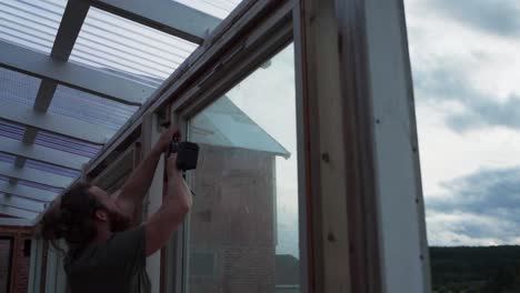 craftsman using cordless electric screwdriver in constructing diy greenhouse