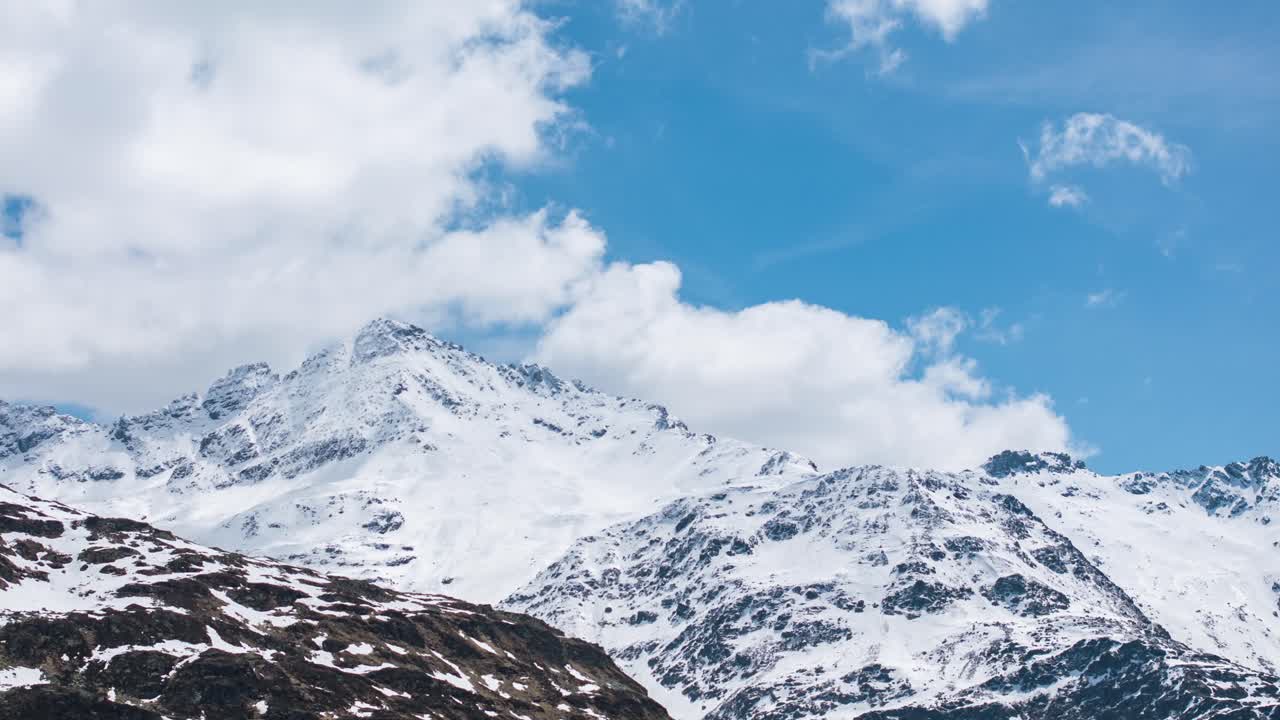 Majestic snow-capped peaks of Montespluga under blue sky with white clouds, Italian Alps, Italy. Time-lapse motion-lapse
