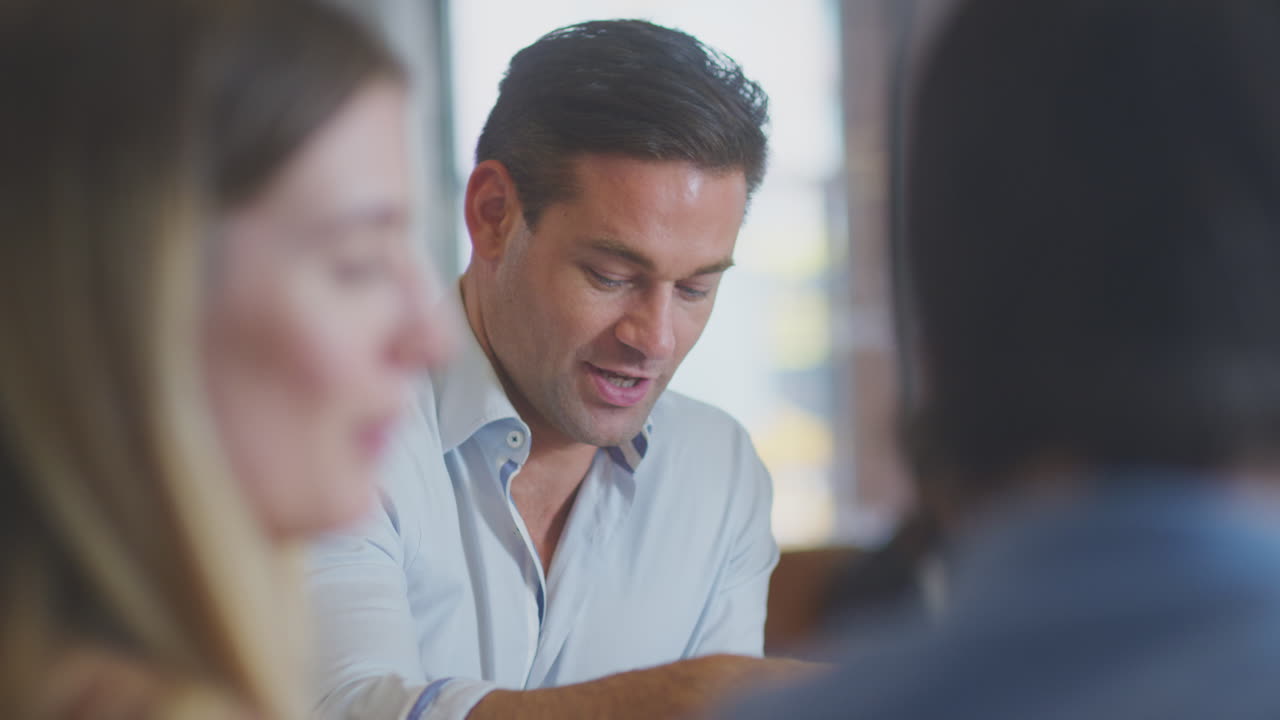 현대 오픈 플랜 사무실에서 테이블 주위에 앉아 회의를 하는 비즈니스 팀의 클로즈업