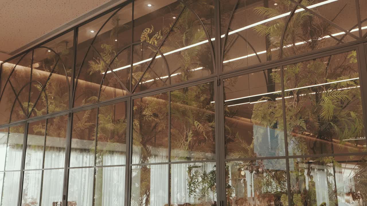 Large arched glass wall reflects foliage and interior lights in elegant wedding venue setting