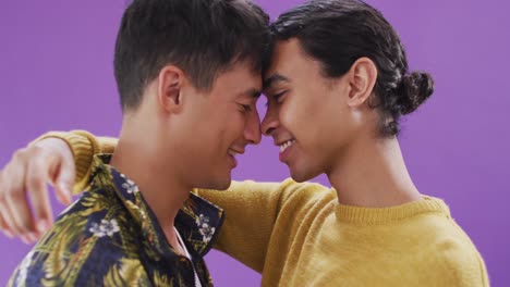pareja feliz diversa tocando las frentes y abrazándose sobre un fondo púrpura