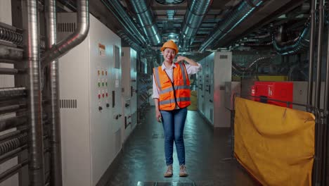 full body of asian female engineer with safety helmet smiling to camera and making call me gesture while standing in engine control room, work of electrical generators