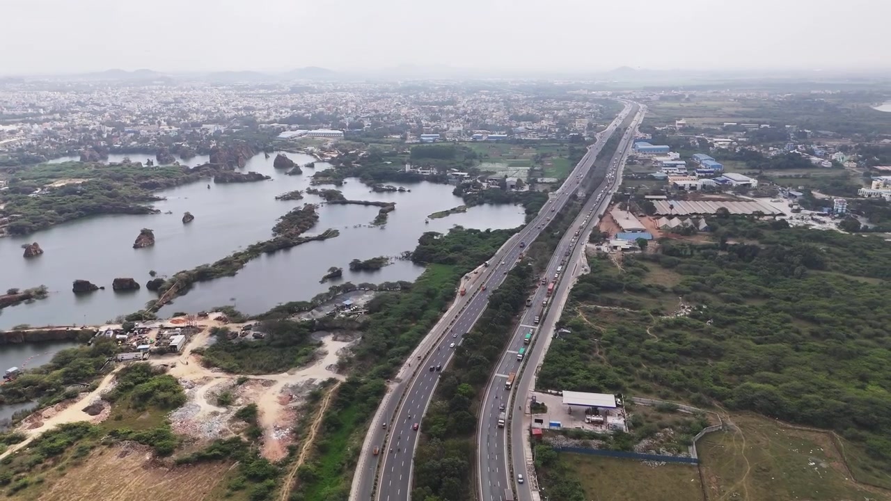 Pemandangan udara Tambang Granit Sikkarayapuram dan Jalan Tol Lingkar Chennai. Danau-danau bekas tambang yang tergenang air, pulau-pulau berbatu, lahan basah hijau, dan lalu lintas jalan raya yang lancar menciptakan perpaduan mencolok antara alam dan buatan manusia.