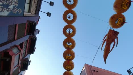 Coloridos-Farolillos-Chinos-Colgando-De-La-Calle-En-Japón-Frente-A-Hermosas-Casas-Japonesas-Bajo-El-Cielo-Azul---Mirando-Hacia-Arriba