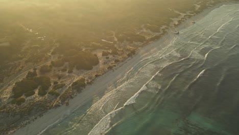 a golden sunset bathes a pristine beach in warm light, revealing gentle waves lapping against the shore and dense vegetation covering nearby sand dunes.