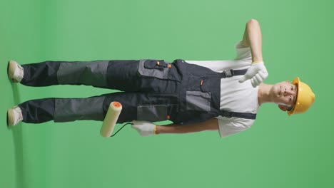 full body of asian man painter wearing safety helmet showing thumbs down gesture to camera while standing in the green screen background studio