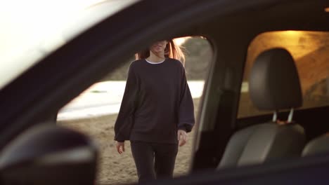 woman in black casual walks to the car through the sea beach, feel relaxed, smiling