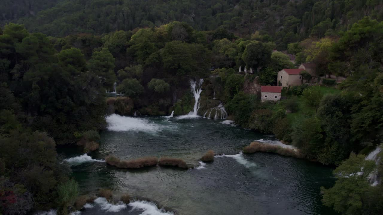 Letecký pohled na vodopád Krka kaskádovitě padající do klidné řeky v bujném lese, Chorvatsko