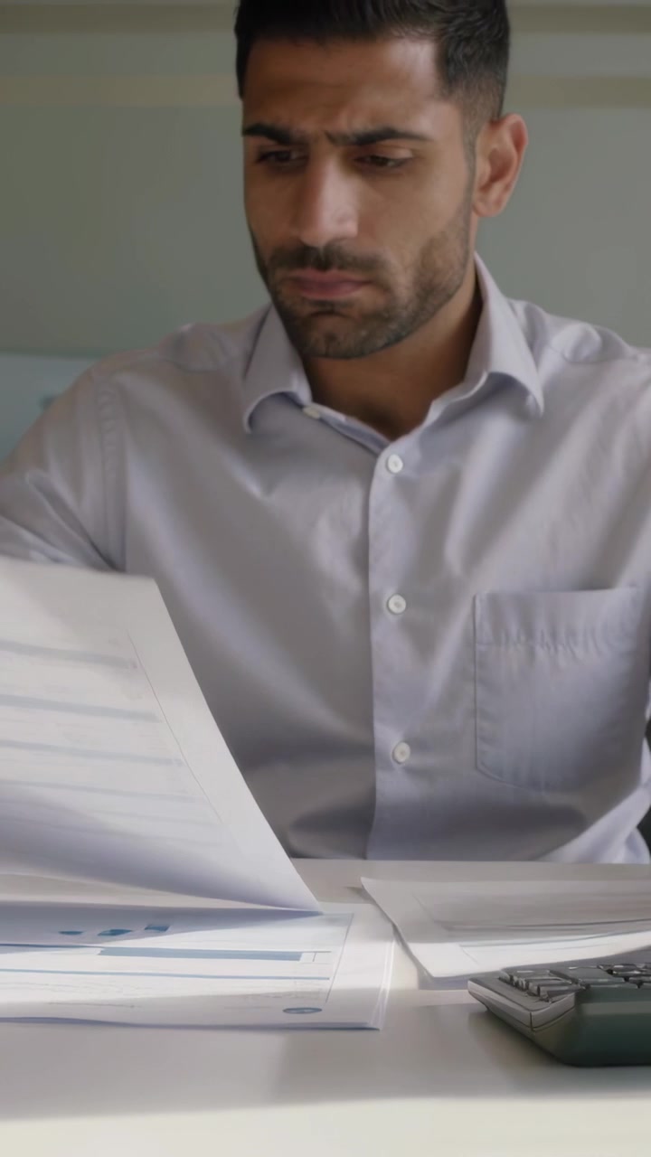 Video verticale: Consultando rapporti, uomo in camicia chiara verifica i totali in ufficio con una calcolatrice