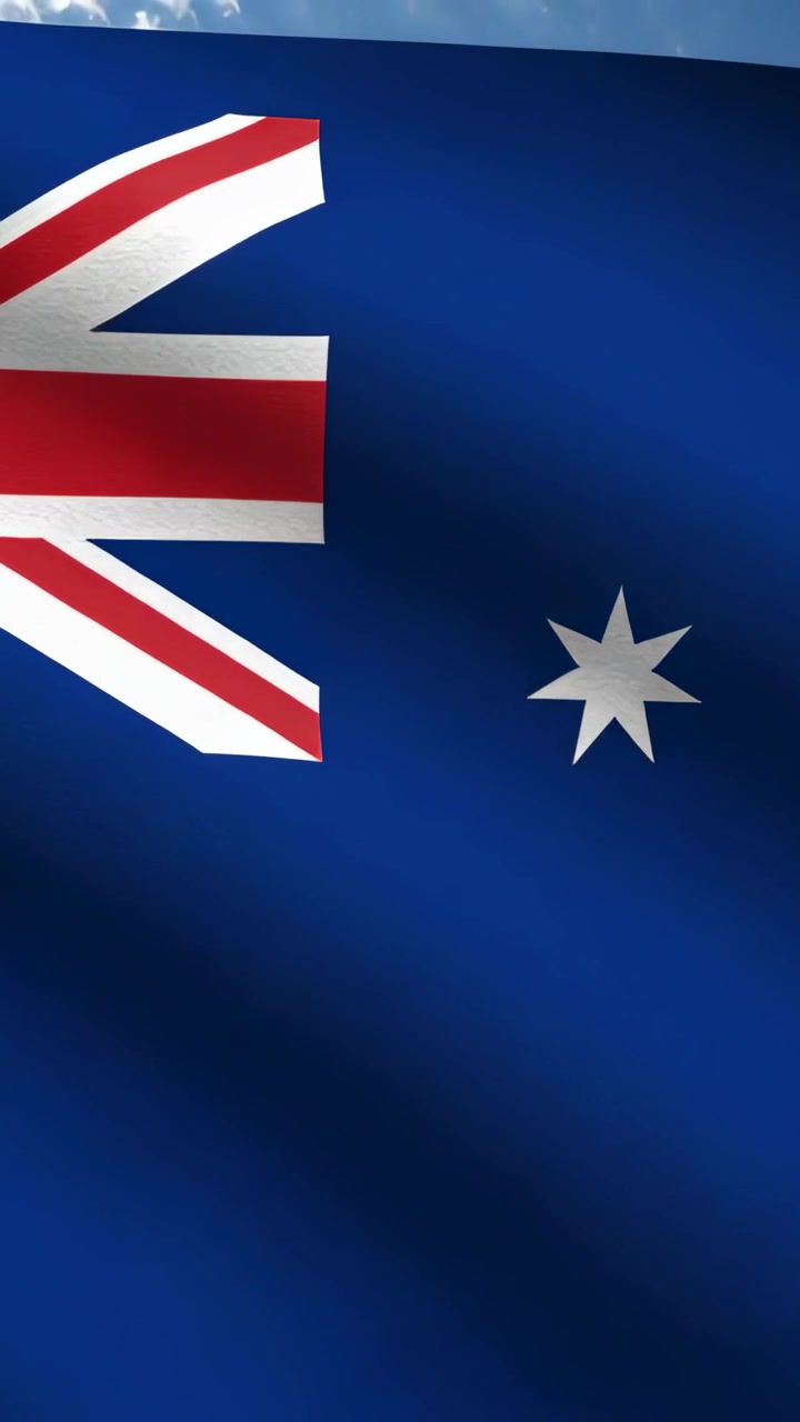 Vídeo vertical: Bandeira australiana ondulando com a brisa, mostrando a Union Jack, estrelas e dobras, com o céu ao fundo.
