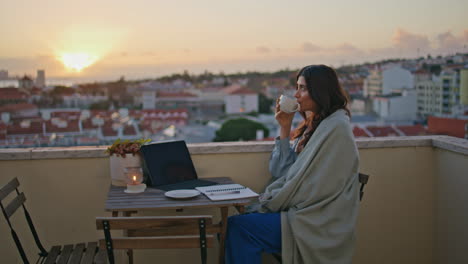 reflective girl sipping cappuccino at sunrise cityscape balcony. woman morning