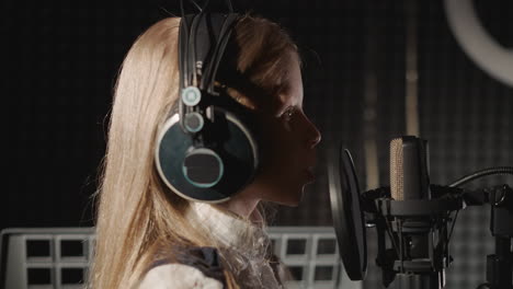 pequeña niña graba una canción en un estudio de audio. joven vocalista canta en el micrófono en el estudio de grabación mientras baila a la música. joven generación de música escénica