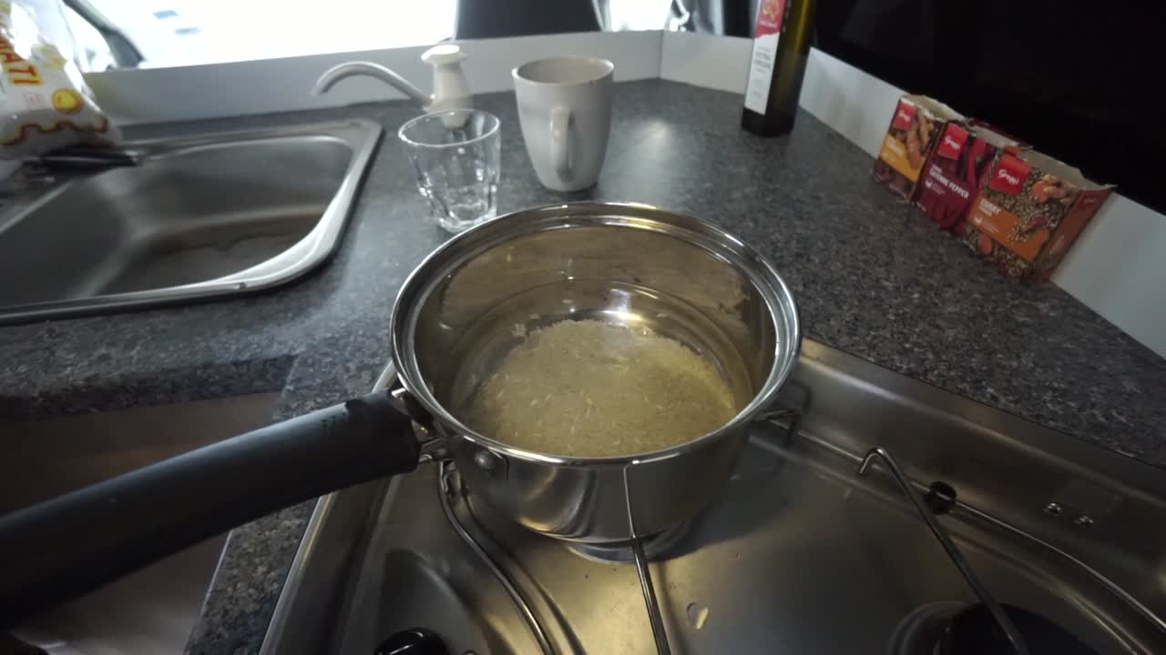 RALLENTATORE - Giovane caucasico/a che aggiunge sale in una pentola di riso e acqua nella cucina di un camper.