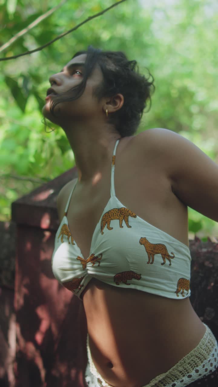 Woman posing outdoors in jungle-inspired bikini top, looking up peacefully