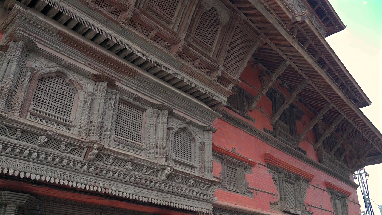 Un'inquadratura statica a bassa angolazione e media distanza che mostra file di finestre in legno intagliate finemente e antica architettura Newar su una parete di palazzo in mattoni rossi a Kathmandu, Nepal