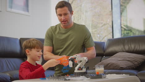 father and son wearing pyjamas building robotic arm from plastic kit at home for science project - shot in slow motion