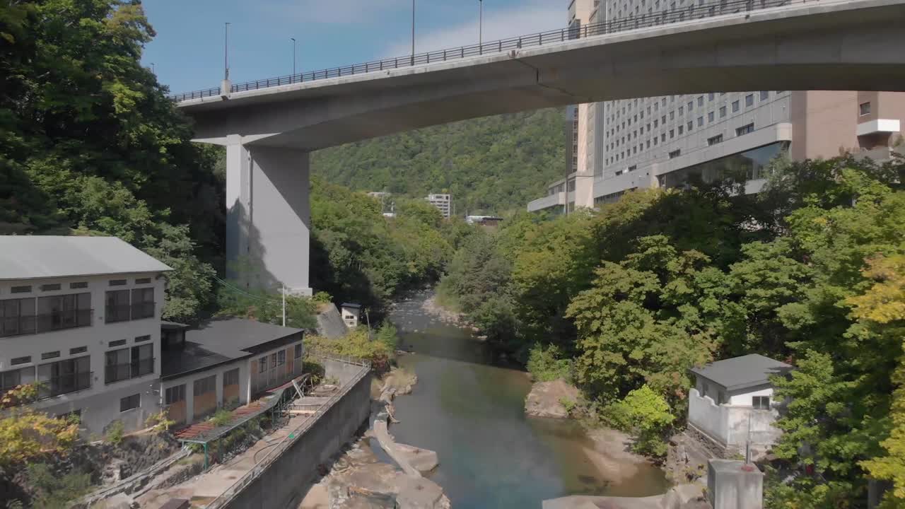 Aerial shot passing over bridge above river in Jozankei famous hot spring onsen town in Hokkaido, Japan