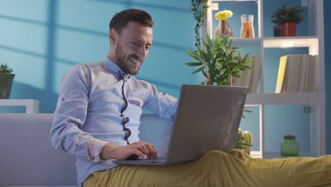 hombre adulto guapo de pelo rubio carismático usando una computadora portátil, sentado en la sala de estar en casa.