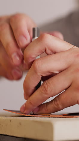 leathersmith makes holes in workpiece with special fork at table in shop closeup. craft manufacture of leather accessories. traditional manual craft