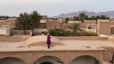 una chica asiática del medio oriente usa bufanda y camisa de color granada rojo galaxia azul caminando en la antigua casa club histórica antigua hecha de adobe y ladrillos de barro por el diseño de arquitectura tradicional iran yazd