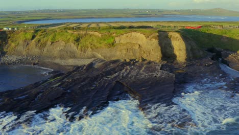 aerial pan of the rocky shore near the bridges of ross, with waves crashing in sunrise light