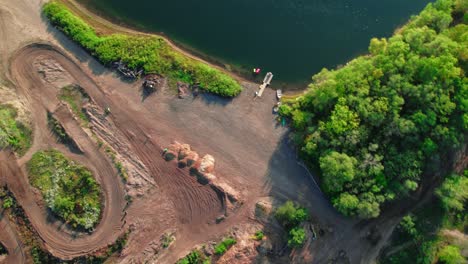 Vista-Aérea-De-Arriba-Hacia-Abajo-De-Pistas-De-Motocross-Para-Motos-De-Cross-Junto-A-Un-Lago-Y-Un-Bosque