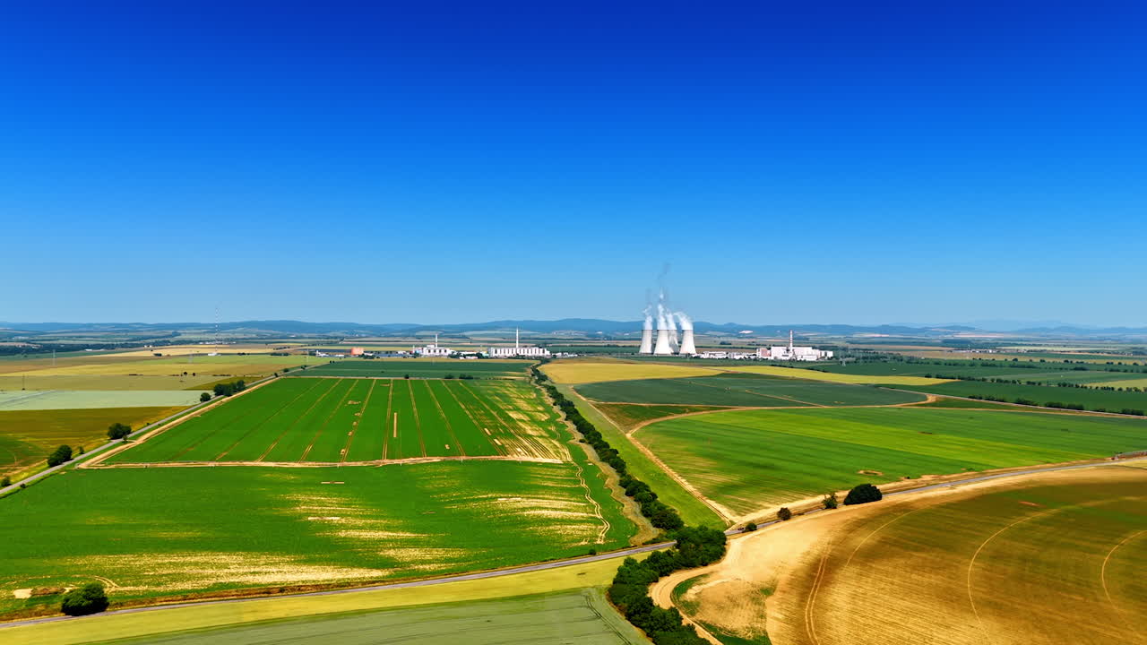 Vast farms and power plant. Green fields stretch across the landscape with a distant power plant visible under a clear blue sky