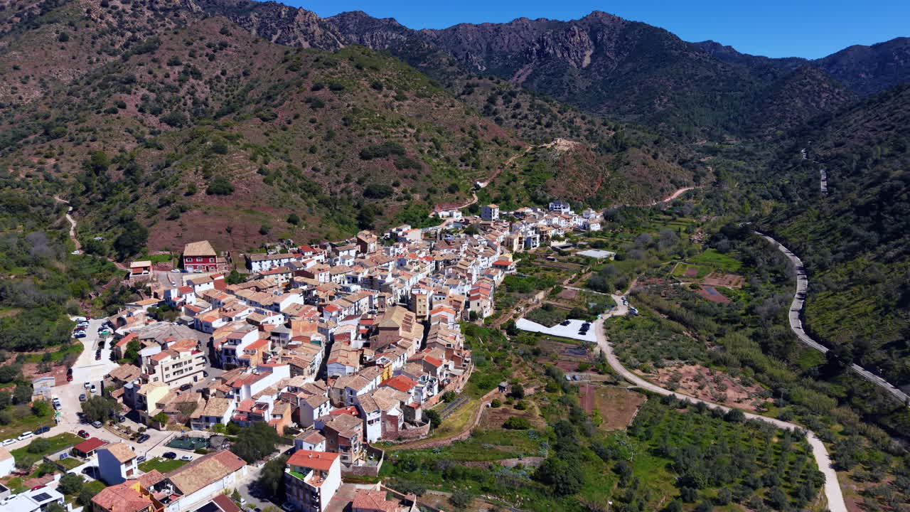 Villaggio di Almedijar incastonato nelle montagne della Sierra de Espadan, Spagna, con edifici dai tetti bianchi e in terracotta circondati da verdi pendii boscosi.
