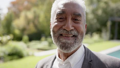 portrait of happy senior biracial man looking at camera and smiling in garden, slow motion