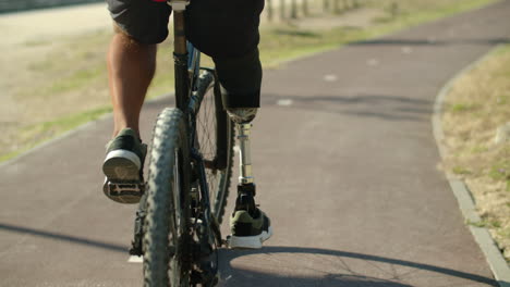 Back-view-of-man-with-disability-riding-bicycle-in-public-park