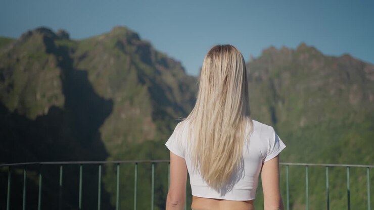 Blond fit woman walking towards steel railing at mountain viewpoint