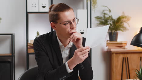 serious businessman sitting at home office desk with letter reading bad news upset and disappointed