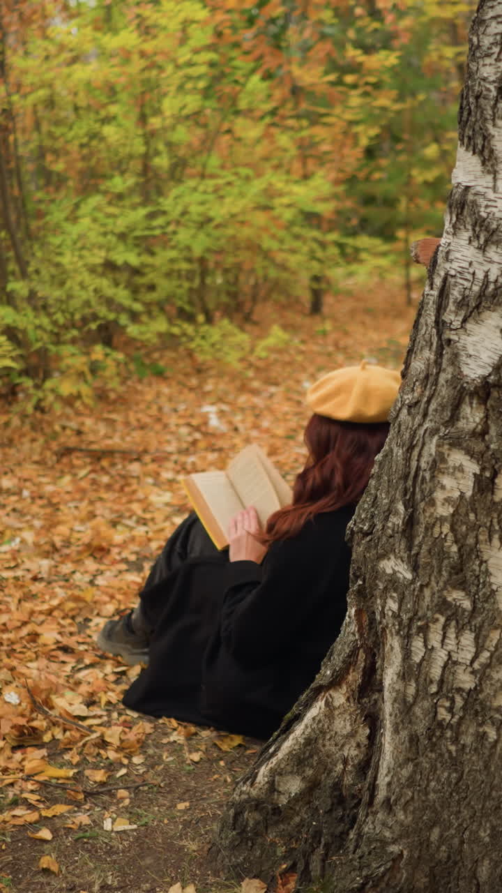 mujer inmersa en el libro, hojeando páginas en la tranquila soledad, apoyada en un árbol en el bosque dorado del otoño, disfruta de la literatura y la serenidad, rodeada de hojas caídas y la belleza de la naturaleza