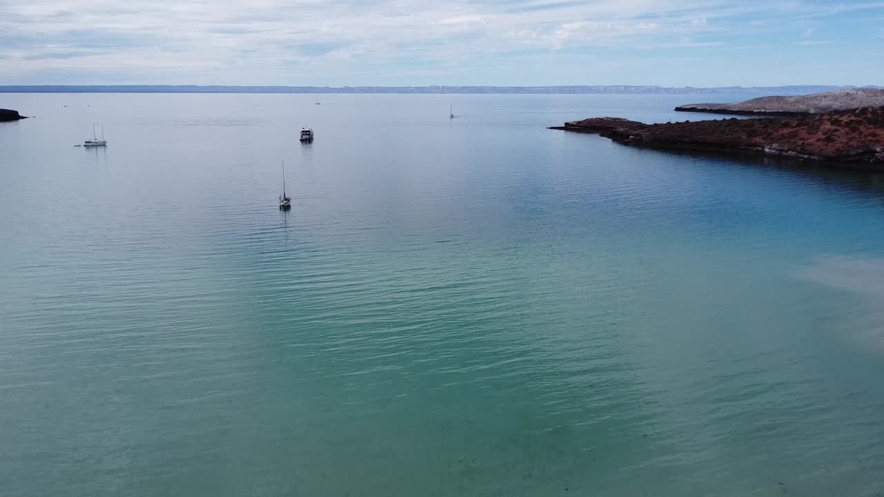 멕시코 바야 캘리포니아 남부 라 파즈의 페리 및 크루즈 항구 근처에 있는 플라야 피치링구 (playa pichilingue) 의 내려오는 공중 사진. 떠다니는 선박과 웅장한 바위 풍경으로 넓은 평온한 바다를 내려다보고 있습니다.