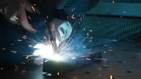 close-up welder wearing protective mask working on metal with a welding machine, sparks and flashes, super slow motion