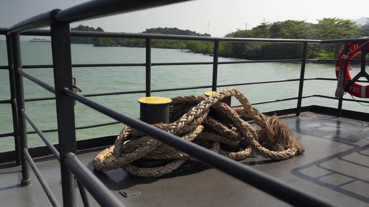 Thick rope tied up on ferry transport vessel surrounded by metal safety fence. Koh Samui, Thailand.