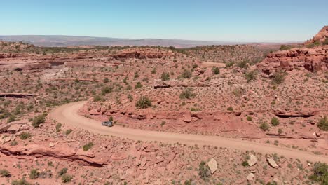 Aerial:-Vehicle-drives-on-dirt-road-in-dramatic-red-rock-canyon,-Moab