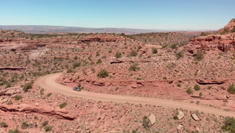 aerial: vehicle drives on dirt road in dramatic red rock canyon, moab